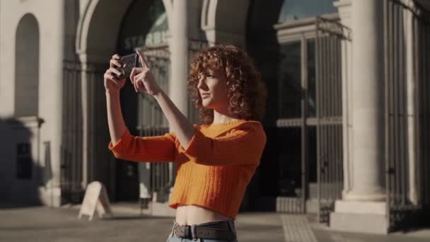 かわいい女性がヨーロッパの市内中心部でスマートフォンの写真を撮る — ストック動画