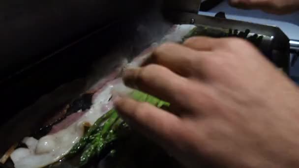 선장은 그릴에서 아스파라거스와 베이컨을 요리한다 — 비디오