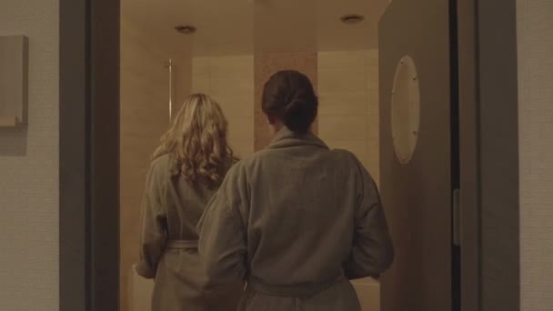 バックビューの二人の女性がバブルバスルームに入り バスローブを脱ぐスローモーション — ストック動画