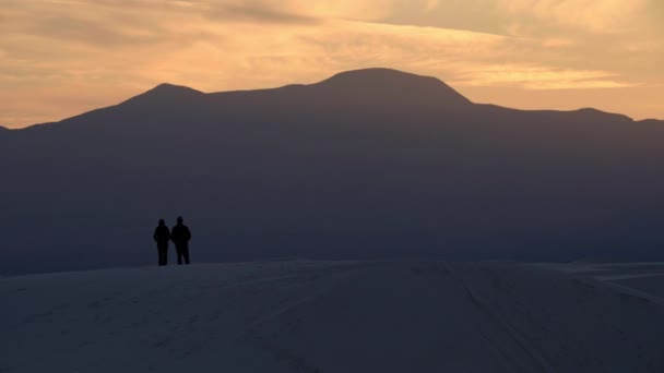 Silhouetted couple stand on hill and watch sunset over majestic mountains, 4K
