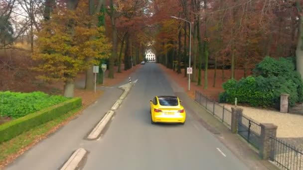 Drone following yellow fancy electric sports car driving down road in woodlands. Tesla Lithium battery EV sustainable travel.