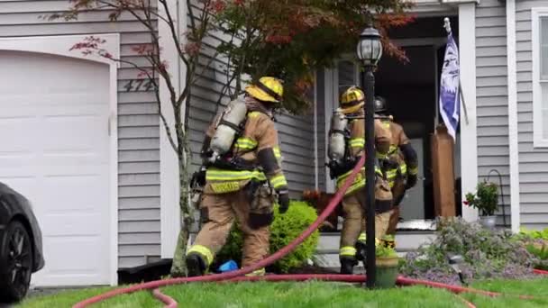 Drie Volledig Uitgeruste Brandweerlieden Dragen Een Brandslang Door Voordeur Van — Stockvideo