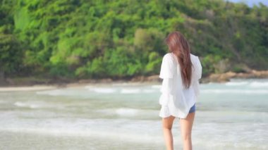 A pretty young woman walks alone in the incoming waves.