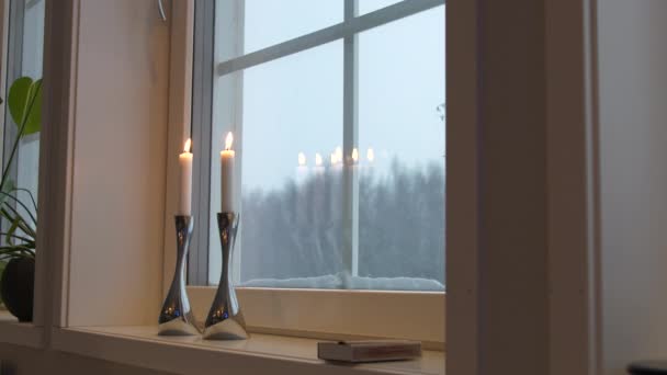 Lit candles on windowsill reflecting on window with snow