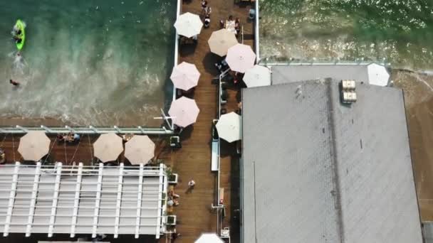 桟橋の端にあるマリブ ファームカフェに向かって桟橋に沿って上に傾いているマリブ ファーム レストランのトップビュー スライティング パンニング アップ ドローンショット — ストック動画