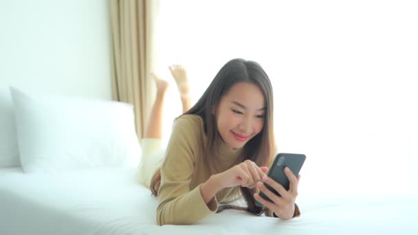大規模な快適なホテルのベッドに横たわっている間 若い女性はデータを入力し 彼女のスマートフォンの画面を交換します — ストック動画