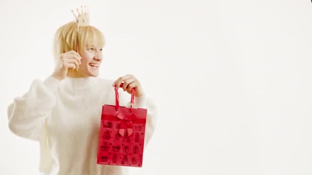 Amused woman having fun with fake crown and bag over white background. Space free for text