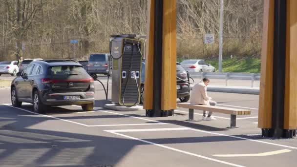 Obchodní muž na lavičce stanice Kontrola jeho Smartphone, Čekání na nabíjení elektrických vozidel