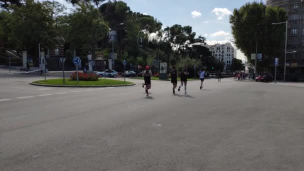 参加马德里年度马拉松赛的选手 地点是阿方索十二世大街 后面有树 路上有车 远处有城市建筑 天上有云 — 图库视频影像