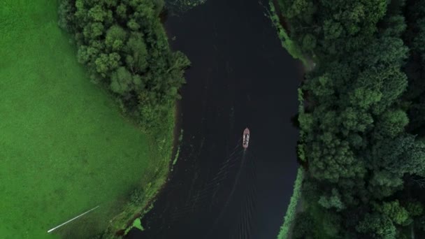 空中上空のドローンカメラ映像では 緑の茂みや木々に囲まれた穏やかなジャングルの川で小さなヴィンテージの木製のスピードボートセーリングを見ることができます ドローンは川やボートの上を飛んでいる — ストック動画