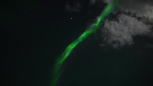 Bottom up shot of green northern light stripe and white clouds against dark sky at night - handheld real time shot
