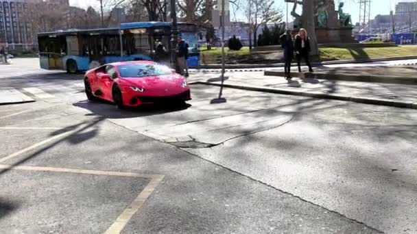 红色兰博基尼汽车驶过布达佩斯市中心 几位游客在阳光灿烂的日子里用手机拍了一张跑车的照片 紧跟在镜头后面 — 图库视频影像
