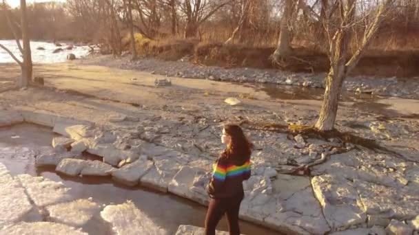 Young Women Wearing Pride Colors Jacket Rock Middle Frozen Lake — Video