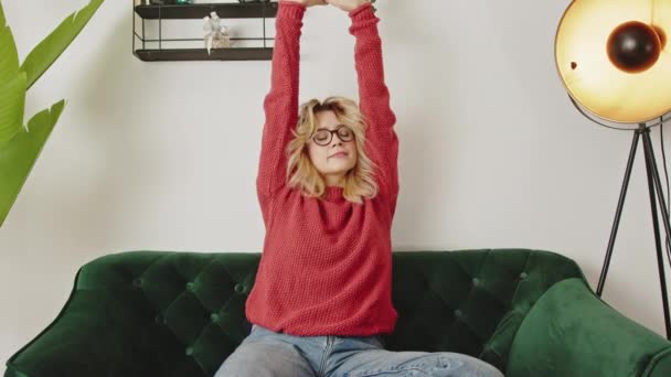 Νεαρό Καυκάσιο Κορίτσι Τεντώματα Σηκώνοντας Χέρια Ενώ Κάθεται Στον Καναπέ — Αρχείο Βίντεο