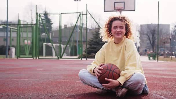 Adorable Teen Girl Sitting Basketball Court Holding Basketball Looking Camera — Stock Video