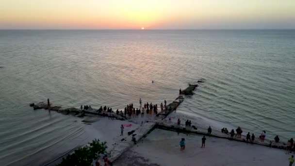 メキシコのHolboxのビーチで夕日を楽しんでいる人々のグループ オレンジと紫の色の空 ドローン軌道撮影 — ストック動画