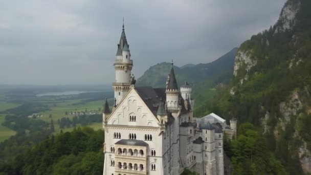 Luftumlaufbahn des malerischen Schlosses Neuschwanstein auf einem Hügel inmitten grüner dichter Kiefernwälder an einem bewölkten Tag, Bayerische Alpen, Deutschland
