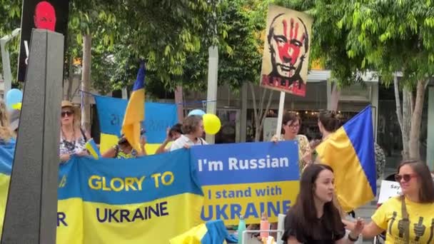 妇女站在一个标有乌克兰国旗的标语牌上 她说我是俄罗斯人 我站在乌克兰一边 其他一些人在布里斯班广场举行的和平集会上高举旗帜和飘扬旗帜 — 图库视频影像