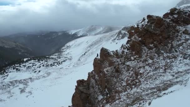 Aerial View Lonely Man Standing Top Rocky Cliff Snow Capped — стоковое видео