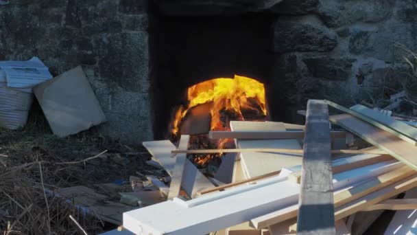 男はオープンキャストの陶芸家の窯で火を準備するために火の上にピッチフォークで松の枝をスローします 静的中射 — ストック動画