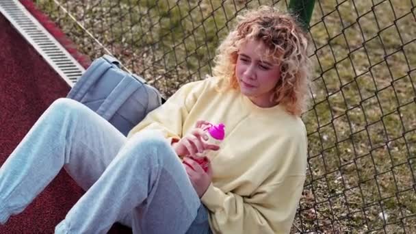 Teenage Caucasian Blonde Girl Sitting Leaning Playground Fence Summer Break — Vídeos de Stock