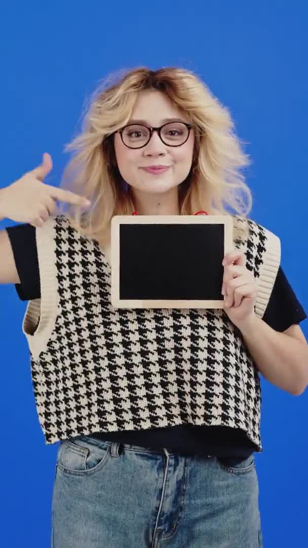 Vertical Video Teenage Caucasian Girl Holding Pointing Small Blackboard Blue — Vídeo de stock