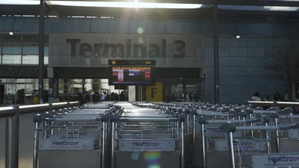 Row Baggage Trolleys Heathrow Terminal Building Airline Departure Board Sun — Stockvideo