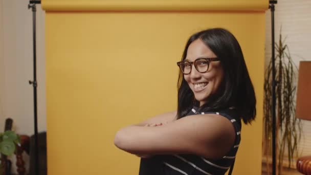 Young Asian Woman Folds Her Arms Smiles Camera Yellow Studio — стокове відео