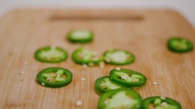 Parlak yeşil jalapeolar ahşap bir kesme tahtasına atılıyorlar, zıplıyorlar ve yığılıp düşüyorlar. 