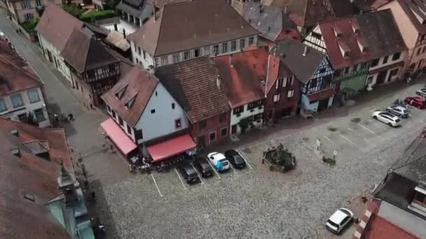 A footage moving onwards across a parking lot within the village. This shot contains streets, a fountain, and parked cars. This is located at the fortified village of Bergheim, Haut-Rhin-France