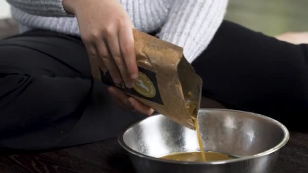 Pouring of dog food meat into bowl from brown paper packet, close up.
