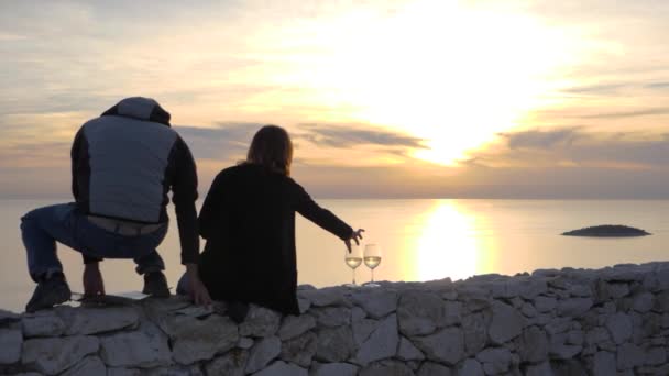 Couple sit on edge to sunset gaze with wine, slow motion.