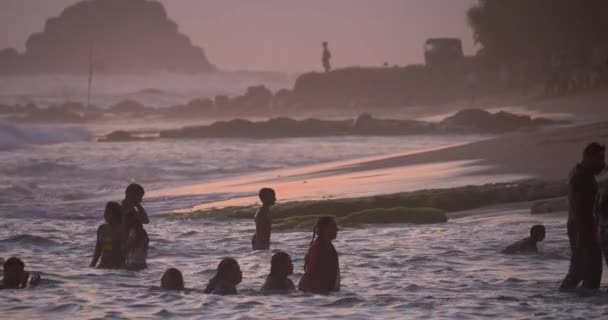 人々は黄金の時間の間に日没時に海でスプラッシュ 空はピンクに塗られている 海岸で波がクラッシュします 水の中に飛び込む少年 — ストック動画