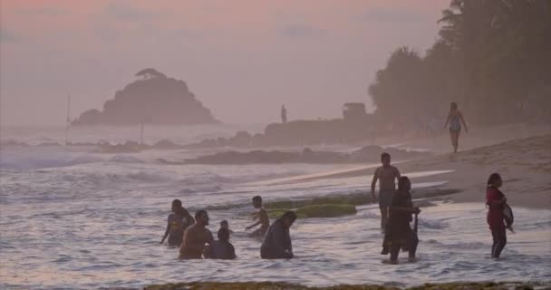 人々は日没時に海に飛び込む 子供たちは水に飛び込む 海岸では波が吹いた 空はピンクに染まっている — ストック動画