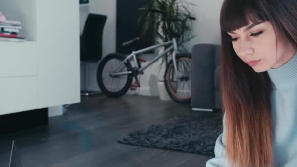 Junge Frau mit langen Haaren sitzt auf dem Boden modernes Wohnzimmer mit E-Bike-Chat-Enthusiasten mit Laptop, Smart House umweltfreundliches nachhaltiges Konzept