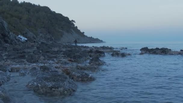 Man Fishing Rugged Island Shoreline Wide Shot — Vídeo de Stock