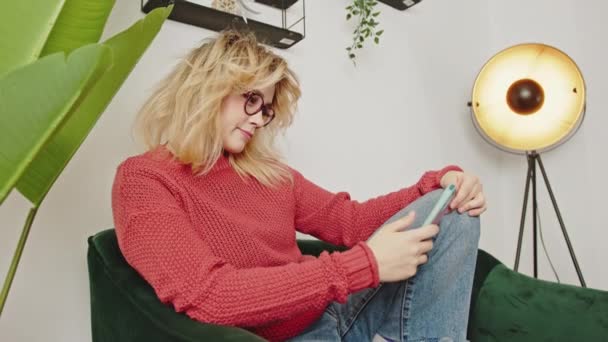 Vídeo Vertical Chica Sofá Con Gafas Lee Teléfono Celular Piensa — Vídeos de Stock