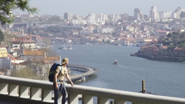 若い愛好家の旅行者のバックパッカーは ドゥオーロ川とポルトガルの有名な都市の素晴らしい街並みの景色をポルトの周りを歩く — ストック動画