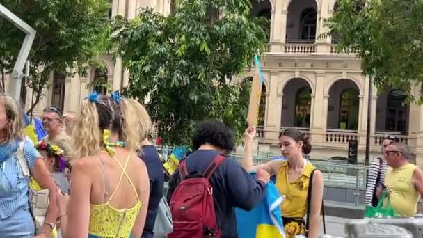 ロシアがウクライナで行った非人道的な特殊軍事作戦に抗議するためにオーストラリアのブリスベン広場に集まった異なる背景の人々のグループをフィーチャーしたパンニング左映像 — ストック動画