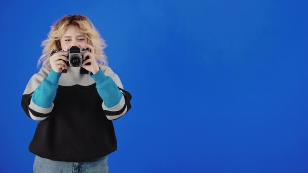 Blondynka Uśmiechnięta Podczas Nauki Fotografii Starą Kamerą Filmową Niebieskie Tło — Wideo stockowe