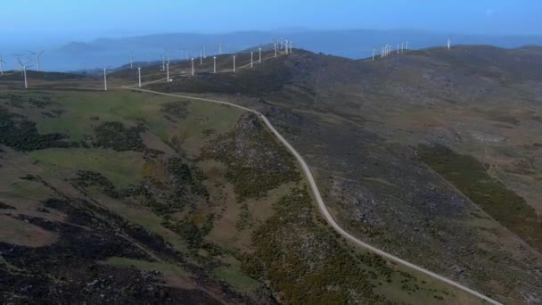 スペインのガリツィアの丘の中腹に回転する風力発電タービンにつながるアクセス道路の上空 ドリー バック — ストック動画