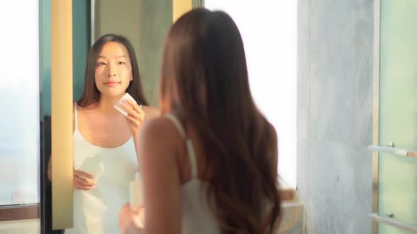 バスルームミラーの前で顔にアンチエイジングスキン製品を適用する美しいアジアの女性 — ストック動画