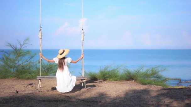 回到摄像机前 一位身穿太阳衣 戴着太阳帽的年轻女子在一个巨大的悬空秋千上摆动着 面对着大海的地平线 标题空间 — 图库视频影像