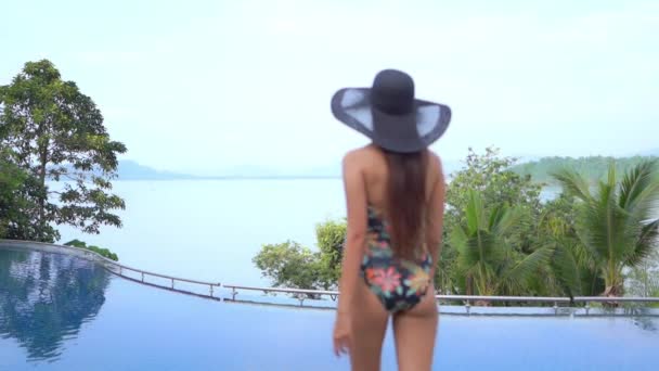 一个穿着印花泳衣 戴着太阳帽的漂亮女人走进镜框 欣赏大海的美景 — 图库视频影像