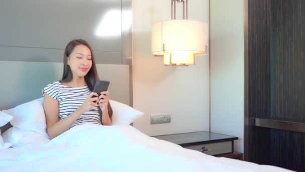 Siedząc Łóżku Młoda Kobieta Uśmiecha Się Sprawdzając Smartfona — Wideo stockowe