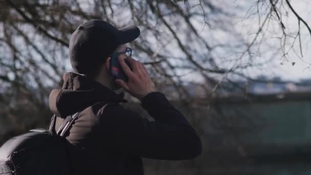 バックパックを背負ったまま携帯電話で話す白人男性 背景の枝 — ストック動画