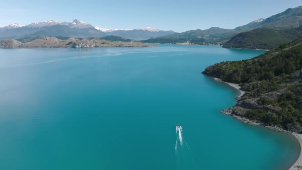 スピードボートで滑らかなターコイズブルーの湖の一般的なカレラで空中飛行過去の海岸線を旅します ドリー フォワードショットの設立 — ストック動画