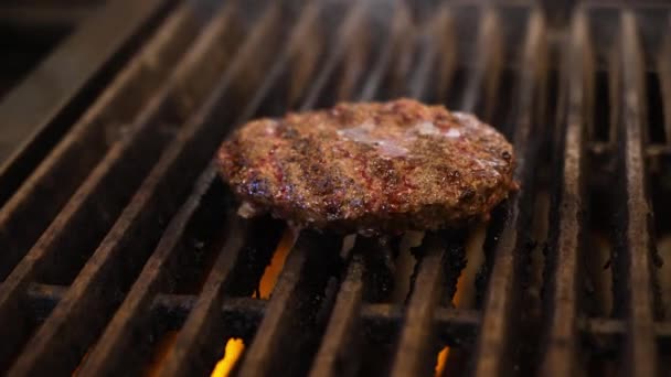 Smoke rises and grease sizzles on grill grates under hamburger patty, slow motion close up 4K