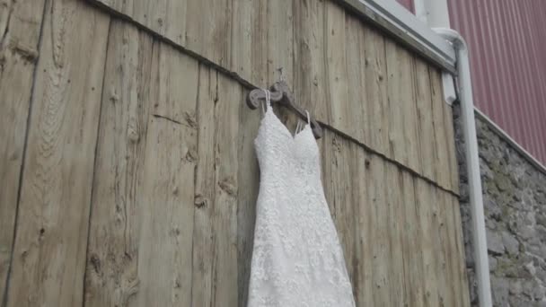 木製の家の壁に屋外にぶら下がっている間 ハンガーのウェディングドレスに向かって映像を移動させます ウェディングドレスは非常にユニークなデザインを持っており それはエレガントに見えます 美しいガウン — ストック動画