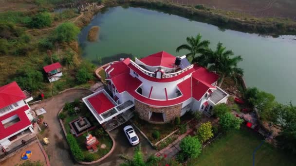 大規模な青い湖に囲まれた休暇のための夏の家の複合体の空中ドローンビューを回転させ インドのVadodaraに駐車場と豊富な緑の植生 — ストック動画